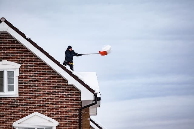  A man shoveling snow off the roof of his house.