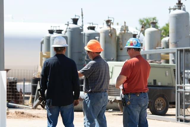 Three men wearing protection helmets on a construction site.